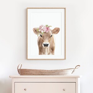 May include: A framed print of a brown and white calf wearing a pink flower crown. The calf is looking directly at the viewer. The background is white.