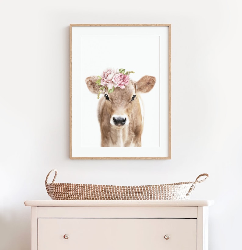 May include: A framed print of a brown and white calf wearing a pink flower crown. The calf is looking directly at the viewer. The background is white.