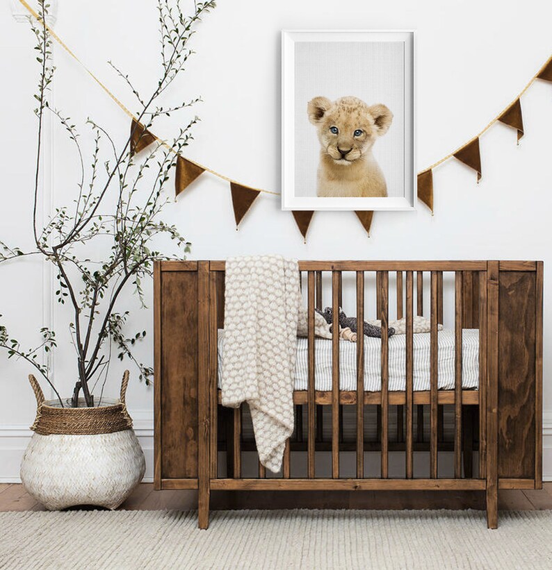 May include: A wooden cot with a white and brown blanket and a white and grey patterned sheet. A framed print of a lion cub hangs above the cot. A brown and gold garland hangs above the cot.