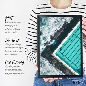 May include: An aerial view of a turquoise pool with swimmers, surrounded by dark rocks and white waves. The image is framed in a black frame with the text "lila-lola" in the bottom right corner.