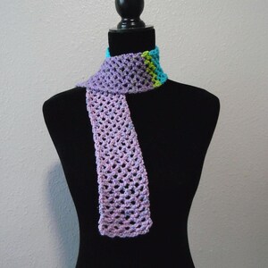May include: A handmade crochet scarf in shades of lavender, blue, and green. The scarf is displayed on a black mannequin. The open weave design and color combination create a unique accessory.