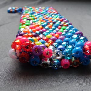 May include: A handmade beaded phone case in a rainbow of colors, including red, pink, blue, green, and purple. The beads are strung together to create a unique and colorful accessory. The case is designed to fit a phone.
