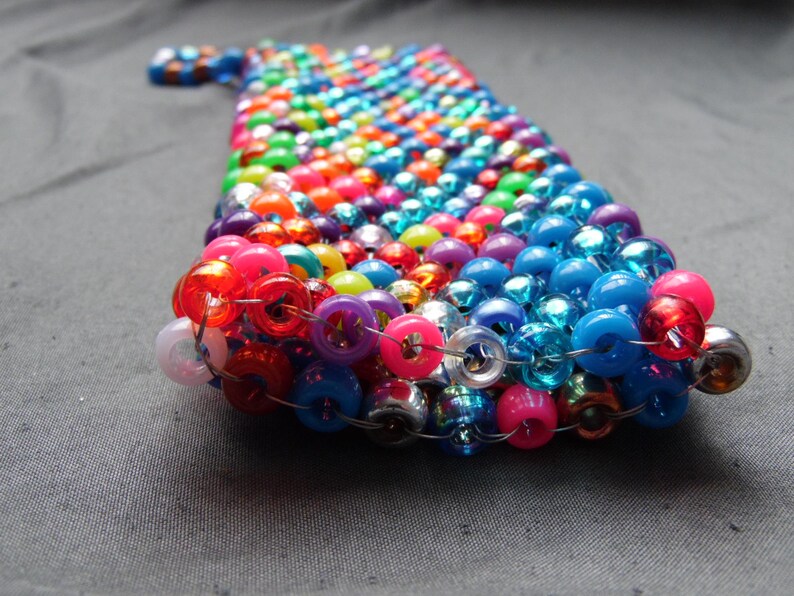 May include: A handmade beaded phone case in a rainbow of colors, including red, pink, blue, green, and purple. The beads are strung together to create a unique and colorful accessory. The case is designed to fit a phone.