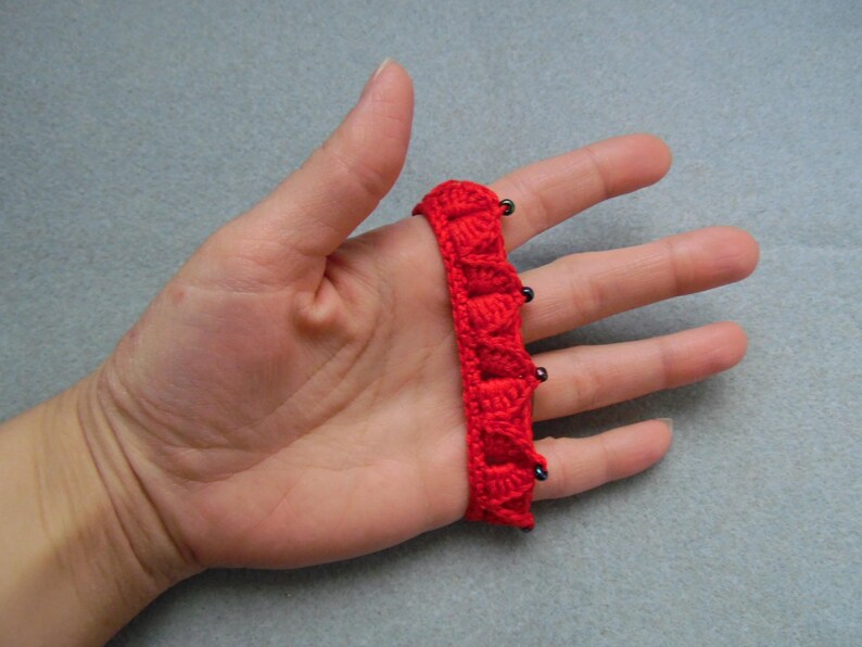 May include: Red crocheted fingerless gloves with black beads. The gloves are worn on a hand.