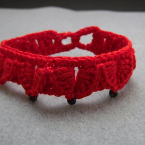 May include: A red crocheted bracelet with black beads. The bracelet is made with a simple stitch and has a delicate, feminine look.