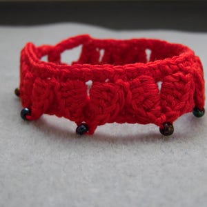 May include: Red crocheted bracelet with black beads. The bracelet is made of a delicate, lacy pattern.