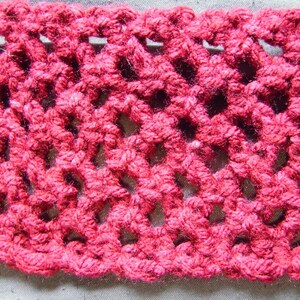 May include: Close-up of a section of hand-crocheted fabric in a vibrant shade of red. The openwork design creates a lacy pattern with visible holes. The texture of the yarn is clearly visible, showcasing the handmade quality of the textile.