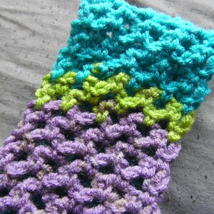 May include: Close-up of a crocheted item with a textured pattern. The item features bands of color, including teal, lime green, and purple. The handmade textile is likely a scarf, hat, or other accessory.