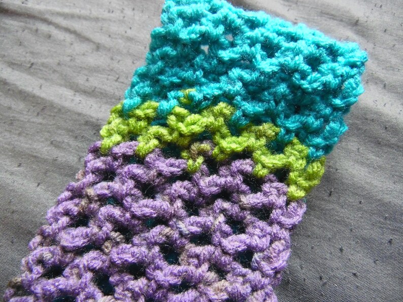 May include: Close-up of a crocheted item with a textured pattern. The item features bands of color, including teal, lime green, and purple. The handmade textile is likely a scarf, hat, or other accessory.