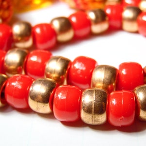 May include: A close-up of a necklace made of alternating red and gold beads. The beads are round and have a smooth finish.