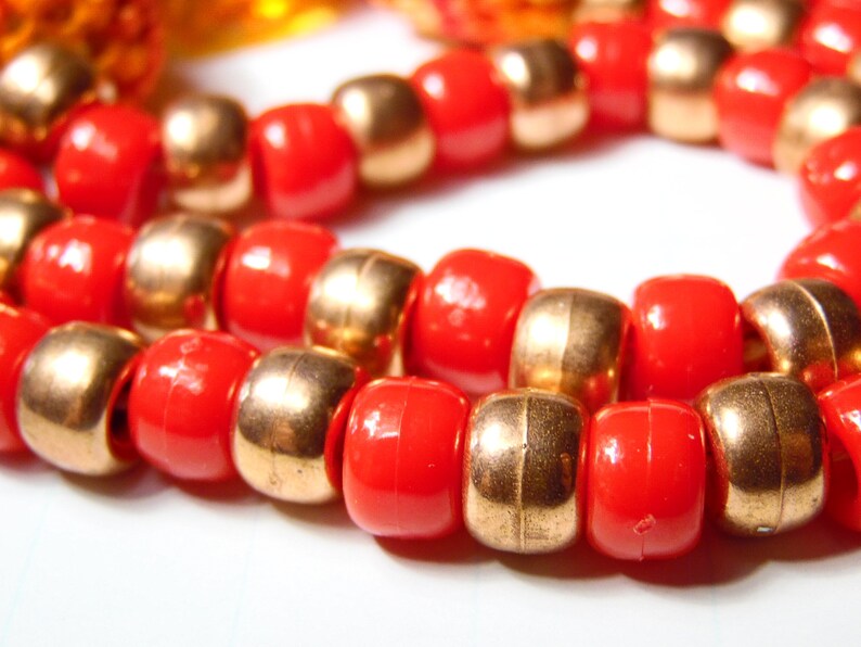 May include: A close-up of a necklace made of alternating red and gold beads. The beads are round and have a smooth finish.