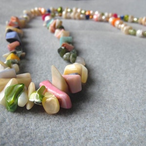 May include: A colorful necklace featuring a variety of natural stone beads in shades of pink, green, yellow, and blue. The necklace also includes a strand of small, round pearls in various colors. The beads are strung together to create a unique accessory.