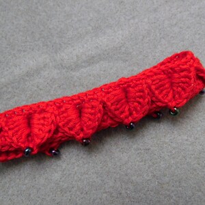 May include: Red crocheted headband with black beads. The headband is made of a soft, textured yarn and has a scalloped edge.