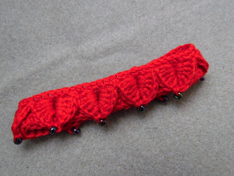 May include: Red crocheted headband with black beads. The headband is made of a soft, textured yarn and has a scalloped edge.