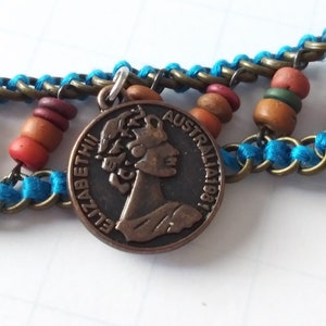 May include: A copper-colored coin pendant with a profile of Queen Elizabeth II and the text "ELIZABETH II" and "AUSTRALIA 1981". The pendant is attached to a blue and brown beaded chain.