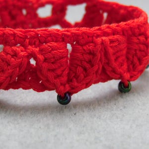 May include: Red crocheted bracelet with black beads. The bracelet is made with a delicate, openwork pattern.