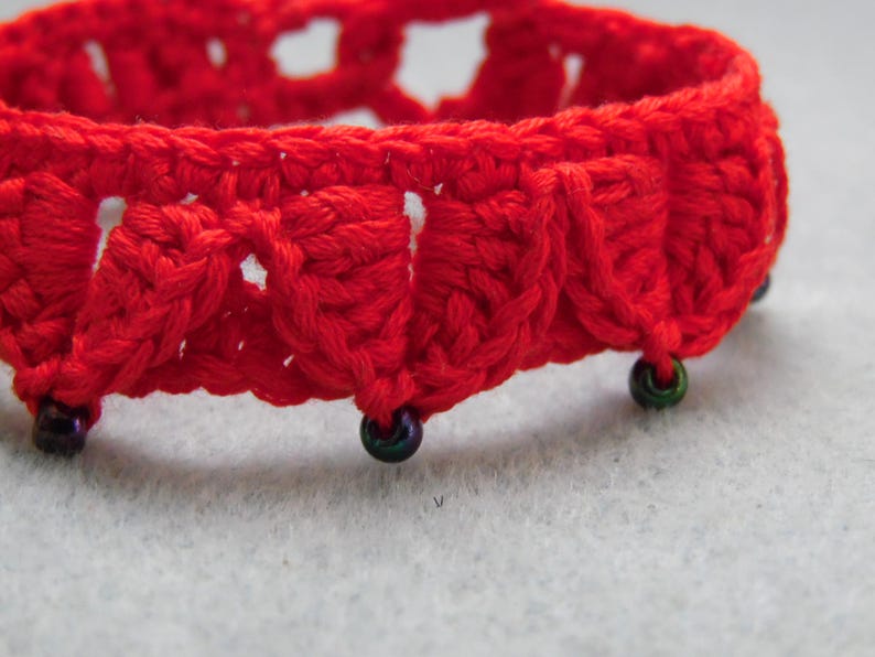 May include: Red crocheted bracelet with black beads. The bracelet is made with a delicate, openwork pattern.