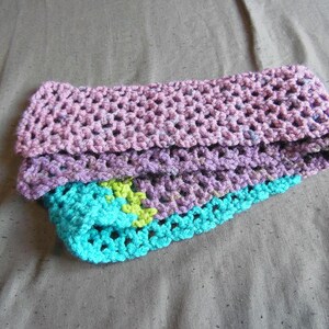 May include: A handmade crochet headband in shades of pink, purple, and turquoise. The headband is folded, revealing layers of textured yarn. A small section of lime green yarn is visible within the turquoise layer.