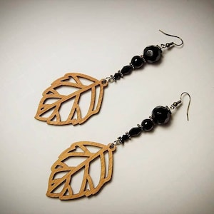 May include: A pair of dangle earrings with black beads and wooden leaf charms. The leaves are cut out and have a natural wood color.
