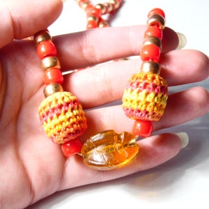 May include: A colorful necklace with orange and gold beads, crocheted yellow and red beads, and a large amber-colored bead.