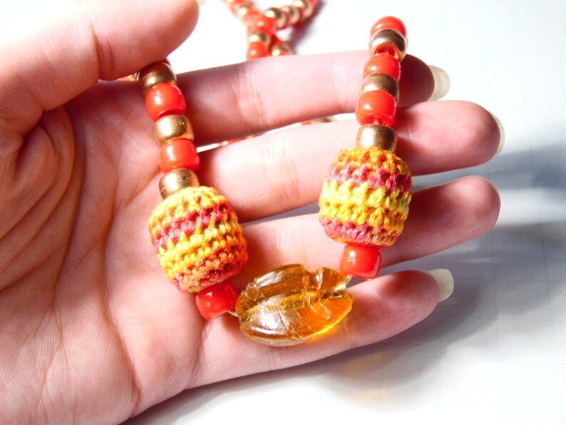 May include: A colorful necklace with orange and gold beads, crocheted yellow and red beads, and a large amber-colored bead.