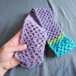 May include: A hand-crocheted scarf in shades of purple, with a turquoise and green border. The scarf is made with a lacy stitch, and the colors blend together. The scarf is approximately 60 inches long.