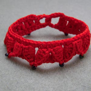 May include: A red crocheted bracelet with black beads. The bracelet is made with a delicate, intricate pattern.