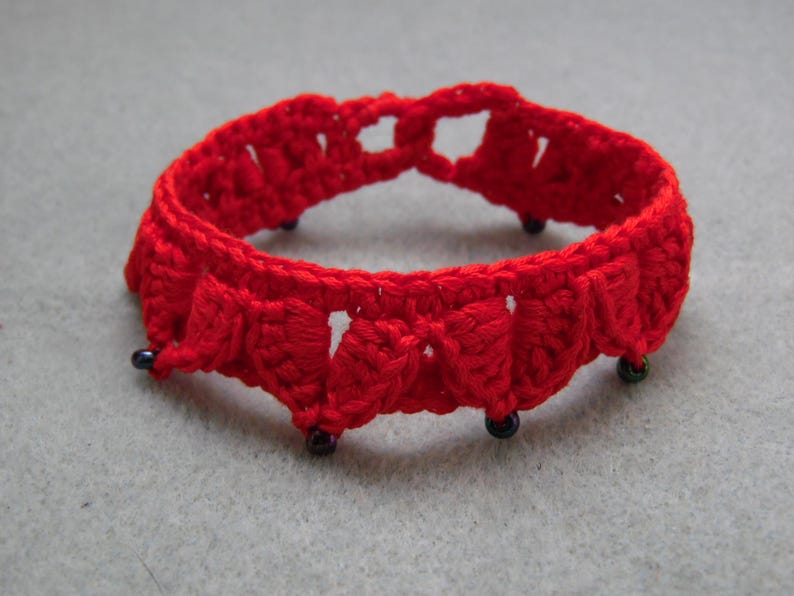 May include: A red crocheted bracelet with black beads. The bracelet is made with a delicate, intricate pattern.