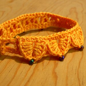 May include: A yellow crocheted bracelet with blue beads. The bracelet is made of a soft, textured yarn and has a delicate, feminine design.