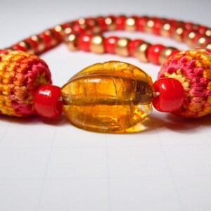 May include: A colorful necklace with red, orange, and yellow crocheted beads and a large amber glass bead.