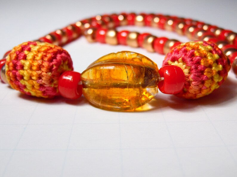 May include: A colorful necklace with red, orange, and yellow crocheted beads and a large amber glass bead.