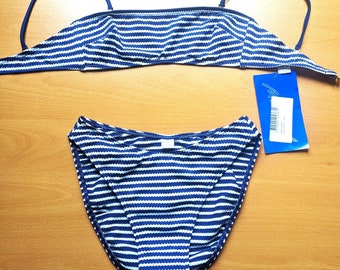 Könnte beinhalten: Zweiteiliger Badeanzug mit blau-weißem Streifenmuster. Das Oberteil ist im Bandeau-Stil mit dünnen Trägern gehalten, und das Unterteil ist klassisch geschnitten. Ein blaues Etikett ist am Set befestigt.