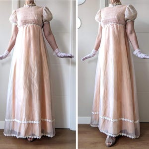 K&ouml;nnte beinhalten: Ein pfirsichfarbenes Empire-Kleid mit hohem, ger&uuml;schtem Ausschnitt und kurzen, gepufften &Auml;rmeln. Das Kleid hat einen transparenten Rock mit wei&szlig;er Spitzenborte am Saum. Das Model tr&auml;gt wei&szlig;e Spitzenhandschuhe.