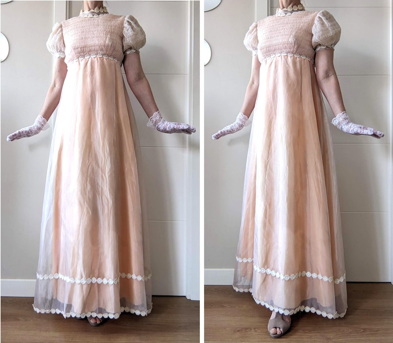 K&ouml;nnte beinhalten: Ein pfirsichfarbenes Empire-Kleid mit hohem, ger&uuml;schtem Ausschnitt und kurzen, gepufften &Auml;rmeln. Das Kleid hat einen transparenten Rock mit wei&szlig;er Spitzenborte am Saum. Das Model tr&auml;gt wei&szlig;e Spitzenhandschuhe.