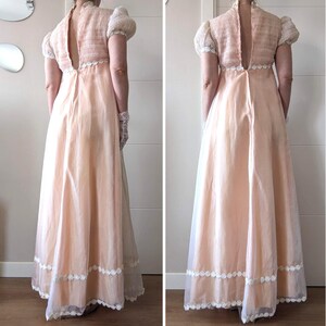 K&ouml;nnte beinhalten: Ein vintage-farbenes Pfirsichkleid mit hohem Ausschnitt und Schl&uuml;sselloch-R&uuml;cken. Das Oberteil hat einen strukturierten Strickstoff mit kurzen, gepufften &Auml;rmeln. Der Rock ist ein flie&szlig;endes, transparentes Material mit wei&szlig;er Spitzenborte am Saum. Das Kleid ist ein klassisches, elegantes Design.