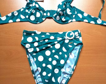 May include: A two-piece swimsuit in teal with a white polka dot pattern. The top is a classic bra style with adjustable straps. The high-waisted bottoms feature a decorative buckle detail. The tag reads "ORY".