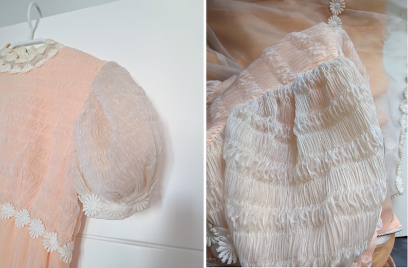 K&ouml;nnte beinhalten: Vintage pfirsichfarbenes Kleid mit transparenten, gepufften &Auml;rmeln. Das Kleid hat einen zarten wei&szlig;en Spitzkragen und eine G&auml;nsebl&uuml;mchen-f&ouml;rmige Verzierung am Saum und an den Manschetten. Der Stoff hat ein strukturiertes, geknittertes Aussehen.