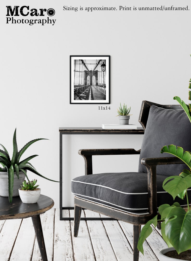 Peut inclure: Photographie en noir et blanc du pont de Brooklyn &agrave; New York. La photo est encadr&eacute;e dans un cadre noir et est expos&eacute;e sur un mur au-dessus d'une table et d'une chaise noires. La taille de l'impression est de 28x36 cm.