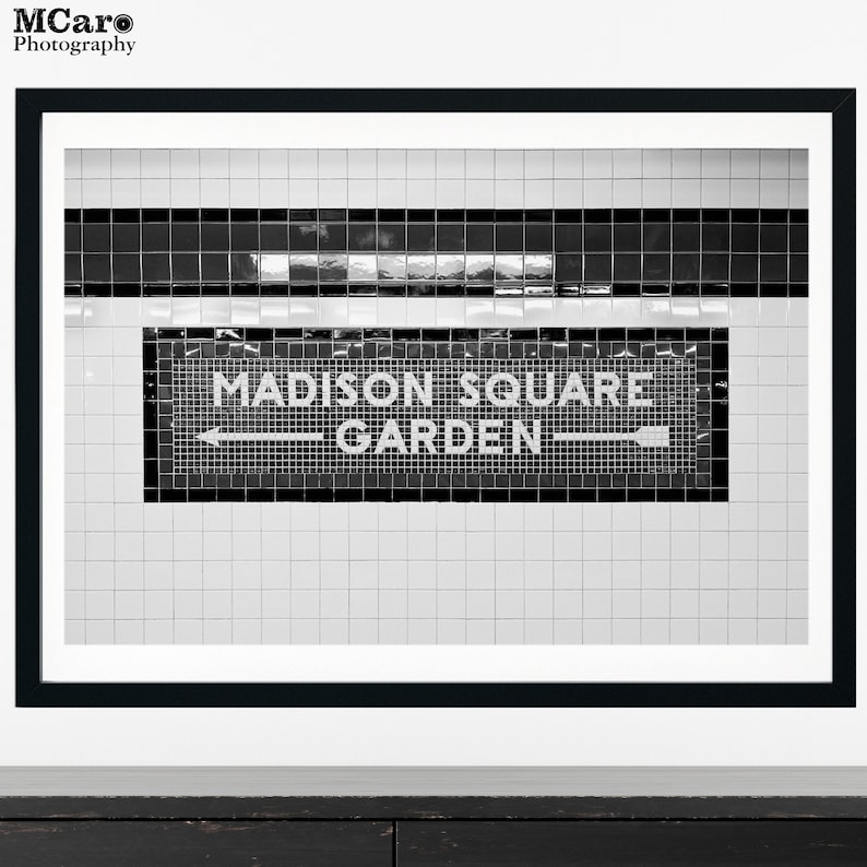 May include: Black and white photo of a subway sign that reads "Madison Square Garden" with a white arrow pointing to the left.