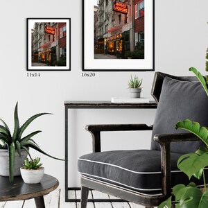 May include: A photograph of a vintage storefront with a neon sign that reads "Wines Liquors". The storefront is located on a city street with brick buildings and a fire escape. The photo is available in two sizes: 11x14 inches and 16x20 inches.