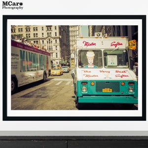 May include: A turquoise and white ice cream truck with the words "Mister Softee" and "The Very Best Softee" on the side. The truck is parked on a city street with other vehicles and buildings in the background.