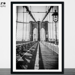Peut inclure: Une photographie en noir et blanc du pont de Brooklyn &agrave; New York. La photo montre la passerelle du pont avec une vue sur les c&acirc;bles et les tours du pont.