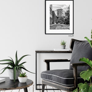 May include: Black and white photograph of the Brooklyn Bridge in New York City. The photo shows a view of the bridge from a street below, with buildings on either side of the street.