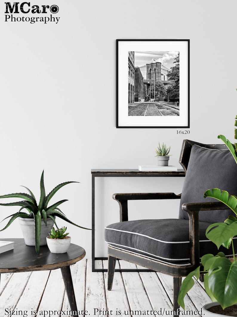 May include: Black and white photograph of the Brooklyn Bridge in New York City. The photo shows a view of the bridge from a street below, with buildings on either side of the street.