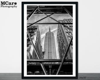 Peut inclure: Une photographie en noir et blanc de l'Empire State Building à New York, vue d'en bas à travers une structure métallique.