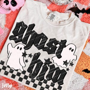 May include: An off-white t-shirt with a black graphic print featuring the text "GHOST him" in a distressed font. The design includes two white ghost illustrations, several black stars, and a black and white checkered pattern at the bottom.