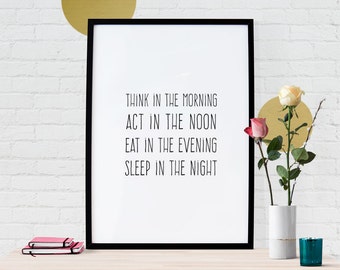 May include: A framed print with the text "THINK IN THE MORNING, ACT IN THE NOON, EAT IN THE EVENING, SLEEP IN THE NIGHT" in black font. A vase with roses and a teal candle sit on a table in front of a white brick wall.