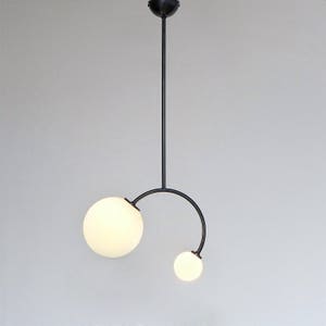 May include: A modern black pendant light fixture with two white frosted glass globes. The fixture features a curved arm that extends from the main stem, holding the smaller globe.