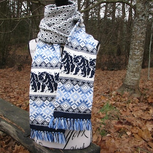 May include: A white, blue, and black knit scarf with a geometric pattern and a fringe. The scarf features a repeating pattern of bears.