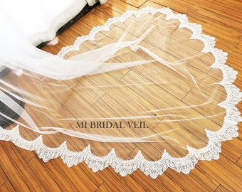 May include: A white bridal veil with a scalloped lace trim. The delicate lace edge frames the sheer fabric, creating a soft, elegant look. The text "MI BRIDAL VEIL" is visible on the veil.